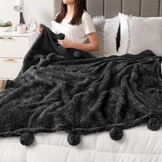 a woman holding a black blanket on top of a bed next to pillows and a night stand