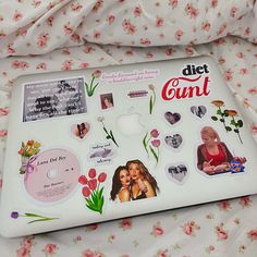 a laptop computer covered in stickers on a bed with pink and white floral sheets