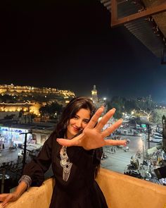 a woman standing on top of a building with her hand out in the air while smiling at the camera