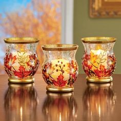 three glass vases sitting on top of a table next to each other with leaves painted on them