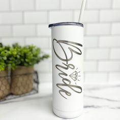 a white tumbler cup sitting on top of a counter next to a potted plant