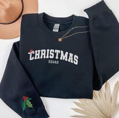 Get ready for the holiday season with our Embroidered Christmas Squad Sweatshirt! Perfect for cozy winter days and festive gatherings, this sweatshirt features "Christmas Squad" embroidered in varsity lettering across the chest, making it a fun and stylish choice for your Matching Xmas shirts collection. The sleeve is adorned with a detailed holly leaf and berries embroidery, adding a unique touch to this Preppy Christmas Sweater. Check out more Christmas items here: https://www.etsy.com/shop/GrumpyGooseApparel?ref=seller-platform-mcnav&section_id=39670071 Browse through my other awesome items here: https://www.etsy.com/shop/GrumpyGooseApparel ABOUT THE PRODUCT: Unisex Heavy Blend™ Crewneck Sweatshirt | GILDAN 18000  A sturdy and warm sweatshirt bound to keep you warm in the colder months. Funny Christmas Sweater, Preppy Christmas, Embroidered Christmas, Funny Christmas Sweaters, Xmas Shirts, Black Christmas, Shirts Funny, Embroidered Hoodie, Fitted Sweater