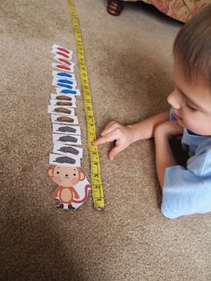 a little boy laying on the floor next to a measuring tape that has animals on it