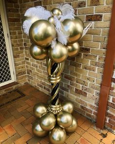 a gold balloon tree with white feathers on it's top and some balls in the middle