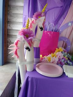 two unicorn - shaped vases with flowers are sitting on a purple table cloth