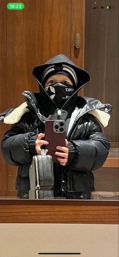 a man in a black jacket taking a selfie with his cell phone while wearing a mask