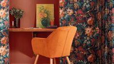 an orange chair sits in front of a desk with a painting and vase on it