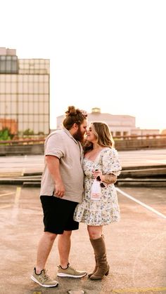 a man and woman standing next to each other in an empty parking lot with buildings in the background