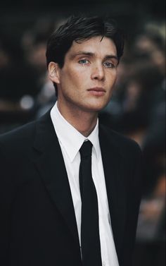 a man in a suit and tie looking off into the distance with people behind him