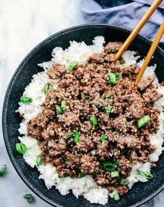 a black bowl filled with rice and ground beef next to chopsticks on the side