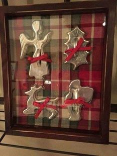 some metal ornaments in a wooden frame with red ribbon on the bottom and one is shaped like an angel