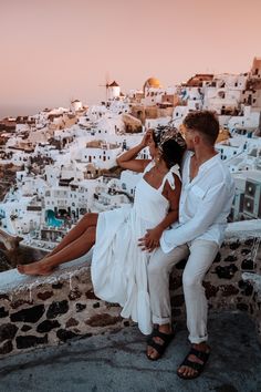 a man and woman sitting on a stone wall next to each other near the ocean