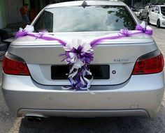 a silver car with purple and white ribbons tied to it's tailpipes