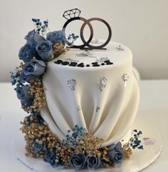 a wedding cake decorated with blue flowers and two rings