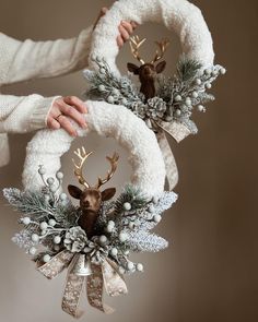 two christmas wreaths with deer heads and pine cones are being held by someone's hands