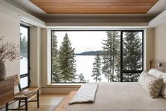 a bedroom with a large window overlooking the water and trees in front of it is shown