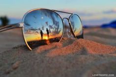 two people are reflected in the mirrored sunglasses on the sand at sunset or sunrise,