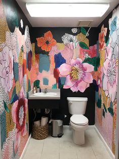 a bathroom with floral wallpaper and two toilets in the same room, one has a basket on the floor next to it