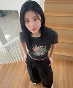 a young woman standing on top of a hard wood floor next to some wooden stairs