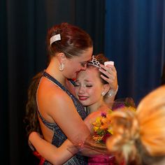 two women hugging each other in front of a blue curtain with flowers on the table