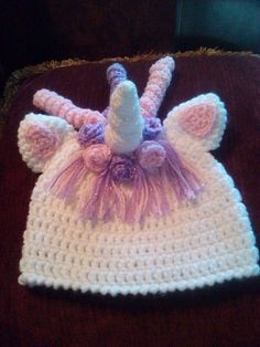 a crocheted white hat with pink and purple flowers on the front, sitting on top of a brown blanket