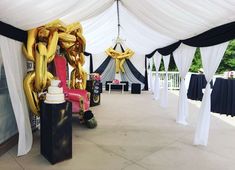 an outdoor event with white drapes and black and gold balloons on the ceiling, along with other decorations