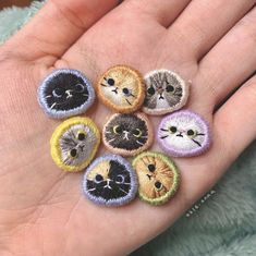 a person's hand is holding six small embroidered patches with different cats on them