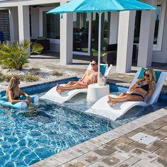 three people sitting in lounge chairs next to a swimming pool with an umbrella over them