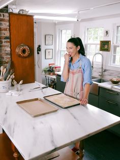 a woman in an apron standing at a kitchen counter with a tray of food on it