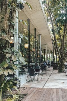 people are sitting at tables in front of trees and plants on the outside of a building