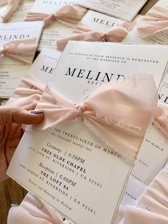 a person holding up a pink bow on top of a wedding card with other cards in the background