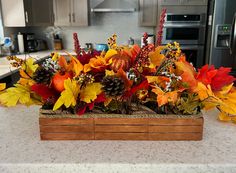 a wooden box filled with lots of colorful fall leaves on top of a kitchen counter