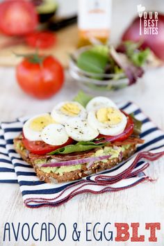 an avocado and egg blt sandwich on a striped napkin with tomatoes, lettuce