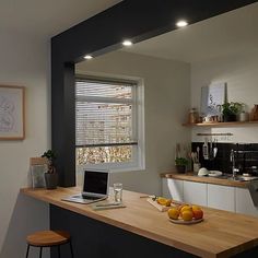 a laptop computer sitting on top of a wooden counter next to a bowl of fruit