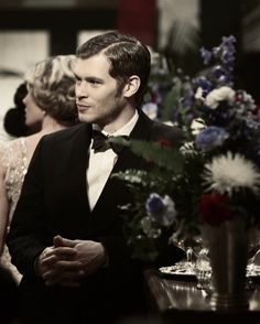 a man in a tuxedo standing next to a woman at a dinner table