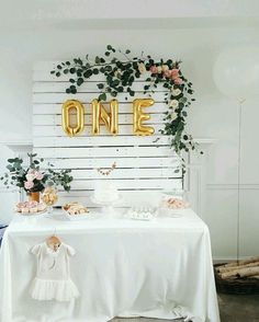 a white table topped with cake and flowers next to a wooden sign that says one