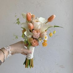 a woman holding a bouquet of flowers in her hand with white and peach colors on it