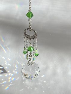 a green and white necklace hanging from a silver chain with crystal beads on it's end