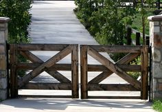 an open wooden gate leading to a walkway with stone pillars and trees in the background