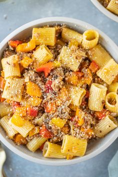 two bowls filled with pasta and meat on top of a blue tablecloth next to utensils