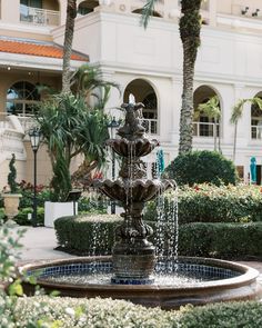 a fountain in the middle of a courtyard with palm trees and bushes around it,