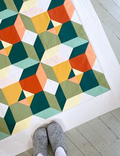 someone is standing on the floor with their feet up in front of a colorful quilt