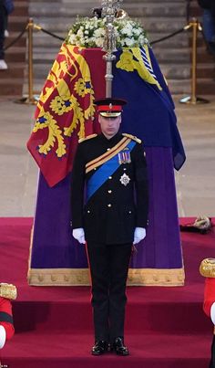 a man in uniform standing next to a purple and red casket with flowers on it