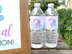 two water bottles sitting on top of a wooden table next to a sign that says mermaid celebration