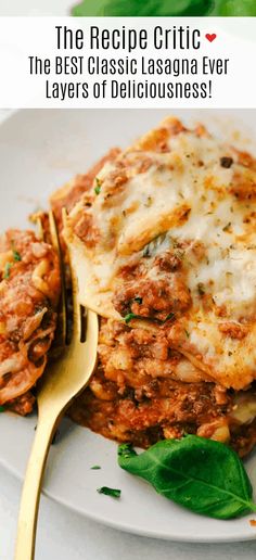 a plate with lasagna covered in sauce and spinach leaves next to a fork