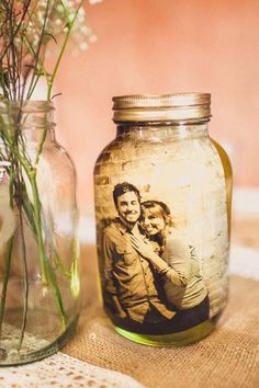 a jar with a photo on it next to a vase filled with flowers and grass