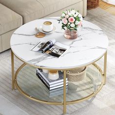 a marble coffee table with magazines and flowers on it in front of a beige couch