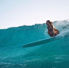 a woman riding a surfboard on top of a wave in the ocean with blue water