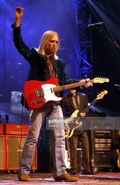 an image of a man on stage with his guitar in the air and one hand up