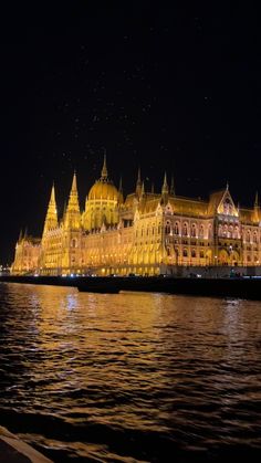 the building is lit up at night with stars in the sky above it and water below